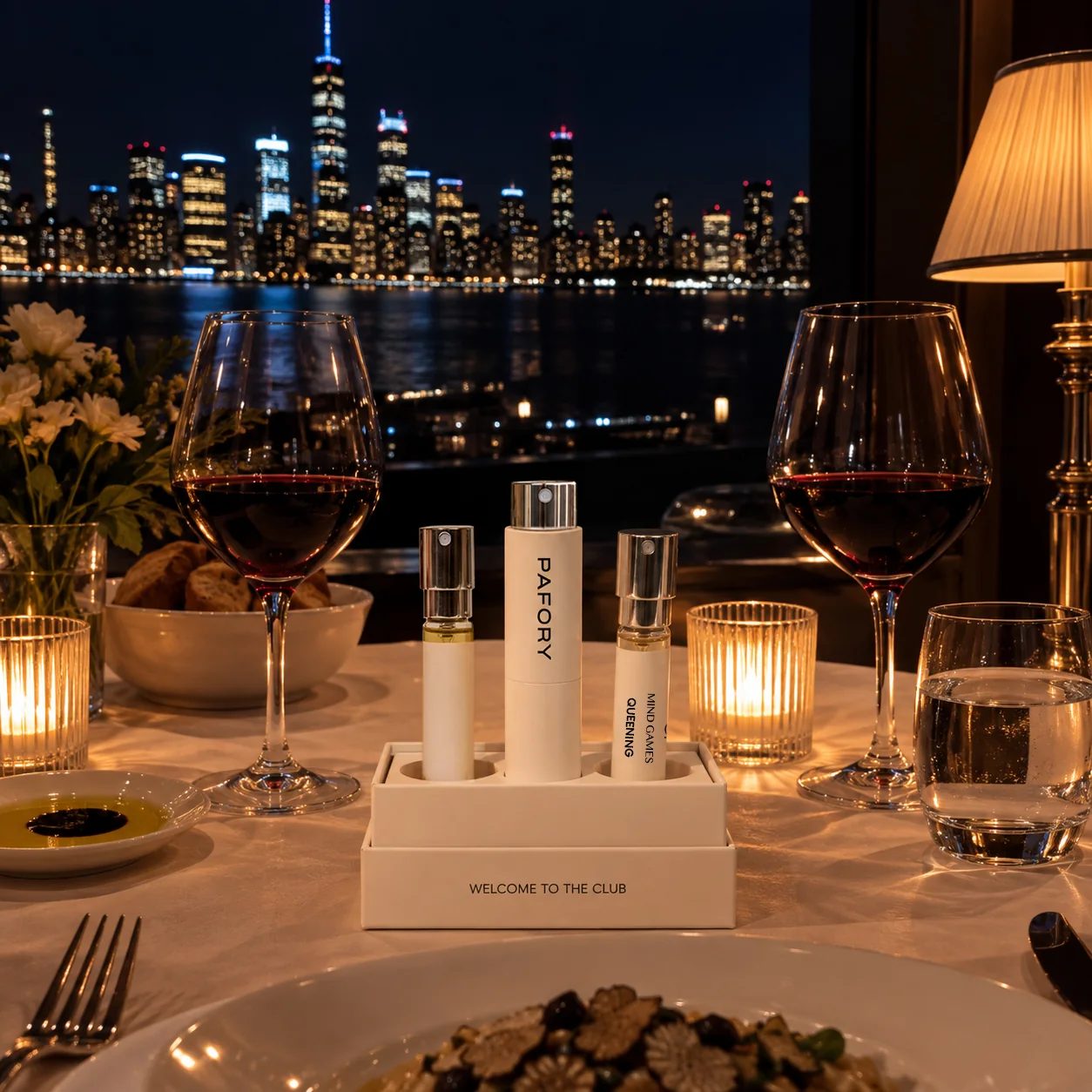 Member Box with the white PAFORY case and the 8 ml Mind Games Queening scent on a candlelit restaurant table, the city skyline at night behind